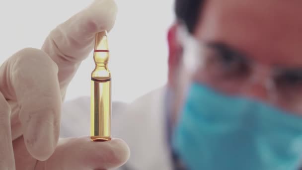 Biomedical researcher watching brown vaccine vial in vertical way - Filmati, video
