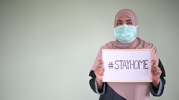 Fiatal gyönyörű muszlim nő orvosi maszk, nézi a kamerát, és azt mutatják rajz "# STAYHOME", hogy megakadályozzák a betegség és a por, pm.5, Maradj otthon karantén coronavírus pandémiás prevenció. Fénymásolási hely. - Felvétel, videó