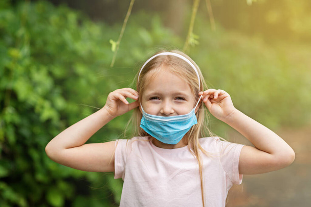 Happy little girl takes off protective medical mask from face outdoors. Victory over coronavirus. The end of COVID-19 Pandemic crisis and lockdown. happiness and hope, stop virus spreading - Fotó, kép