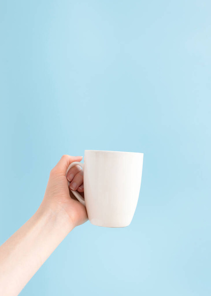 Woman holding white cup on blue background and copy space, vertical. Template mockup mug in hand - Foto, immagini