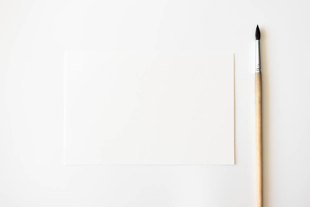 Mockup tyhjä paperi arkki ja sivellin valkoisella pohjalla. Konsepti taidekasvatus, ylhäältä
 - Valokuva, kuva