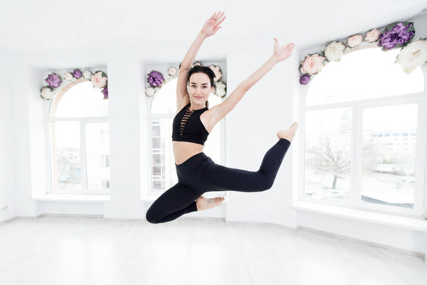 Young slim fitness woman in black sports clothing jumping high on window background - Valokuva, kuva