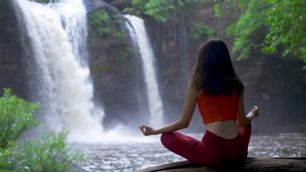 Rear view Asian woman practicing or doing yoga at the waterfall, Lotus pose on meditation session. Beautiful Landscape, Natural background, Thailand. - Footage, Video