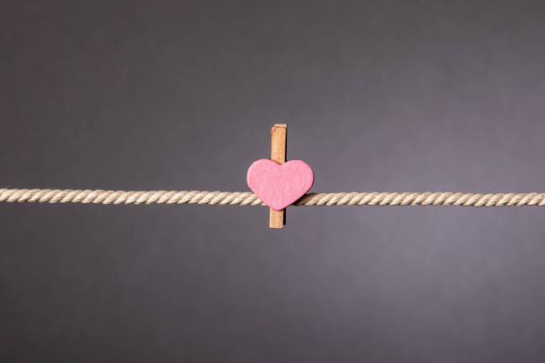 Dřevěné klipy s růžovým srdcem na bílém laně na šedém pozadí - Fotografie, Obrázek