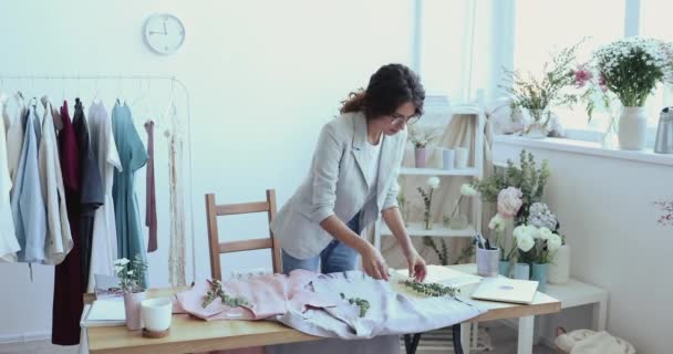 Female fashion designer decorating new custom shirts with green branches - Video, Çekim