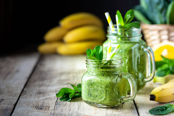 Deux smoothies verts sains aux épinards, banane, orange, pomme, kiwi et menthe dans un bocal en verre et ingrédients. Désintoxication, alimentation, santé, concept alimentaire végétarien. - Photo, image