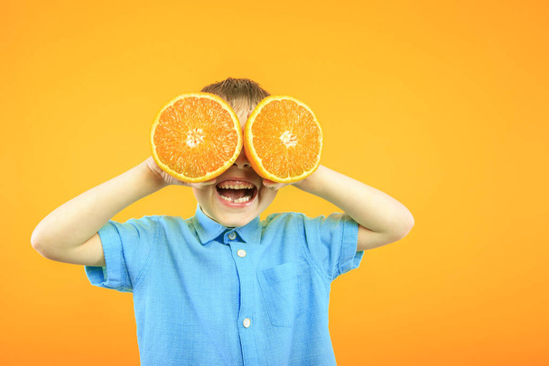 Happy cute boy is having fun played with fruit orange on yellow background wall. Bright photo of a boy. Colored panorama photo. - Foto, afbeelding