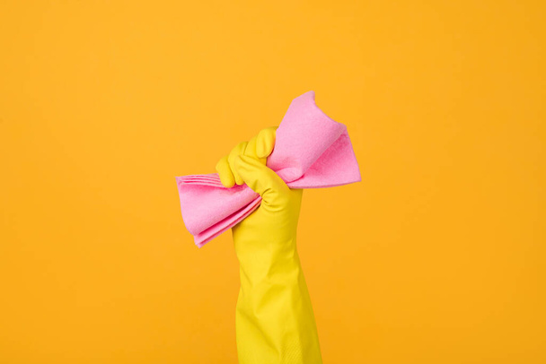 Foto de cerca recortada de una mano en guante amarillo sosteniendo una goma rosa para espolvorear aislada sobre fondo amarillo. Concepto de servicio doméstico
 - Foto, Imagen