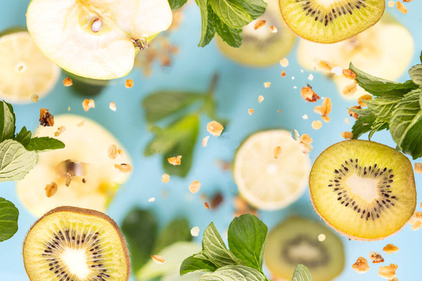 Manzanas, kiwi, limón y hojas de menta en vuelo. Hojas frescas de textura primaveral de diferentes tamaños sobre fondo azul
 - Foto, imagen