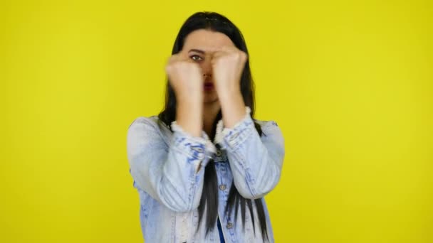 Woman makes a gesture with two hands and smiles on a yellow background - Imágenes, Vídeo