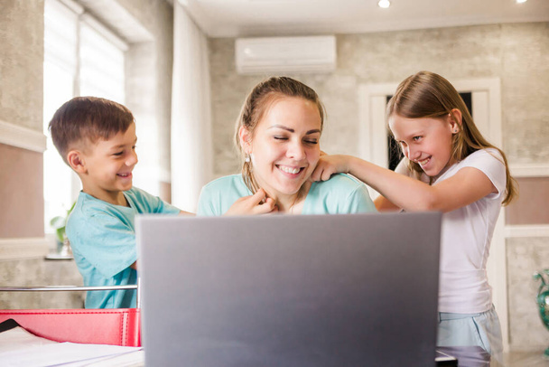 Uma jovem freelancer trabalha em casa remotamente usando um laptop. Mulheres crianças interferir com o seu trabalho, satisfazer e fazer cócegas, pedir-lhe para brincar com eles. Fotografia horizontal
 - Foto, Imagem