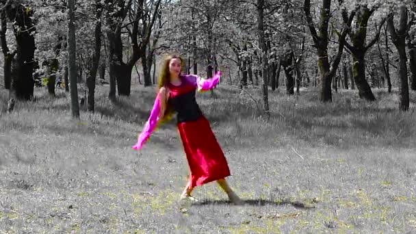 Beautiful young girl with long hair in a red dress is dancing in the forest. - Footage, Video