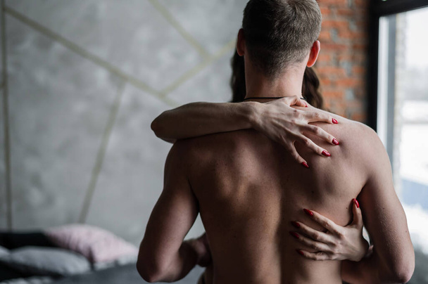 Female hands on the bare back of an unrecognizable man. A young couple cuddles in the bedroom. Love and passion in a relationship. - Foto, Bild