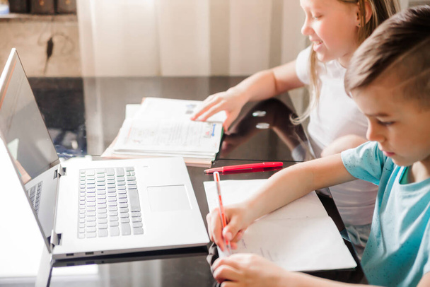 Chlapec a dívka, bratr a sestra studují doma. Děti sedí u stolu s otevřenými zápisníky a notebookem. Vodorovná fotografie - Fotografie, Obrázek