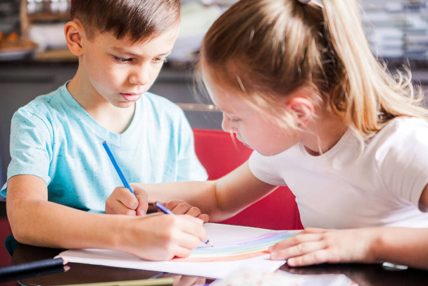 Niño y niña, hermano y hermana dibujan un arco iris con lápices de colores juntos, sentados en una mesa. Fotografía horizontal
 - Foto, Imagen