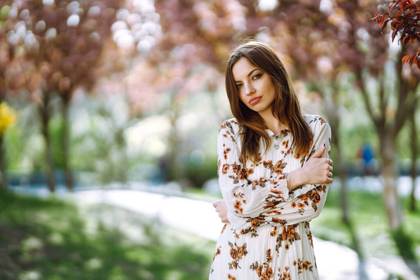 Portrait of attractive woman in a pretty dress with flowers enjoys blooming green garden in spring day. Fashion and style concept. - Фото, зображення