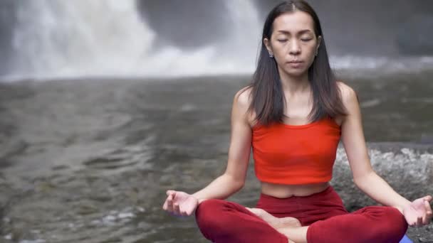 Közelről ázsiai nő gyakorol, vagy jógázik a vízesésnél, Lotus pózol meditációs ülésen. Gyönyörű táj, természeti háttér, Thaiföld. - Felvétel, videó