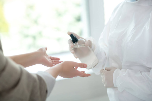 Close-up of medical worker hands spraying antiseptic on female hands - Fotografie, Obrázek