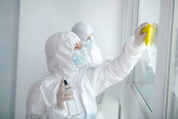 Medical workers in protective clothing and medical masks cleaning and disinfecting window panes - Foto, afbeelding