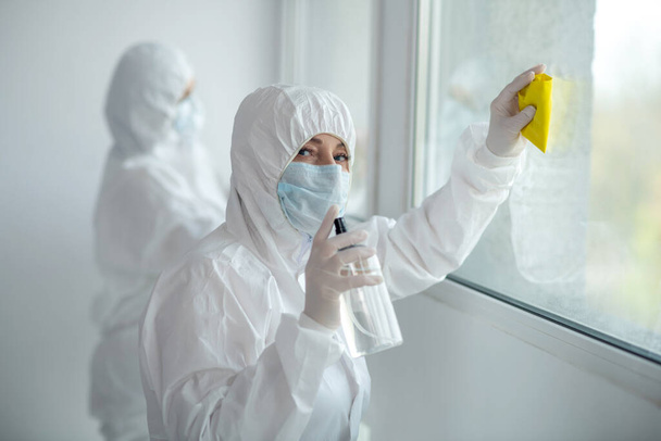 Medical workers in protective clothing and medical masks cleaning and disinfecting window panes - Foto, Imagen