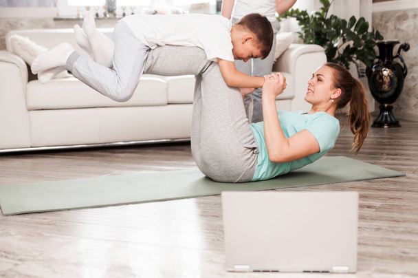 Mãe e filho fazem exercícios esportivos juntos em casa em um tapete de ginástica. O menino retrata um avião. Fotografia horizontal
 - Foto, Imagem