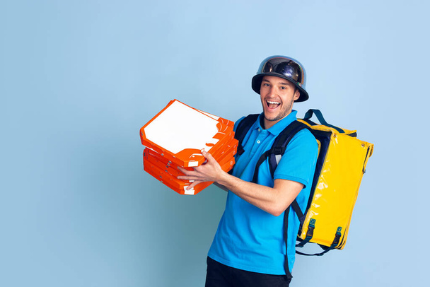 Contacless delivery service during quarantine. Man delivers food and shopping bags during insulation. Emotions of deliveryman isolated on blue background. - Foto, Imagem