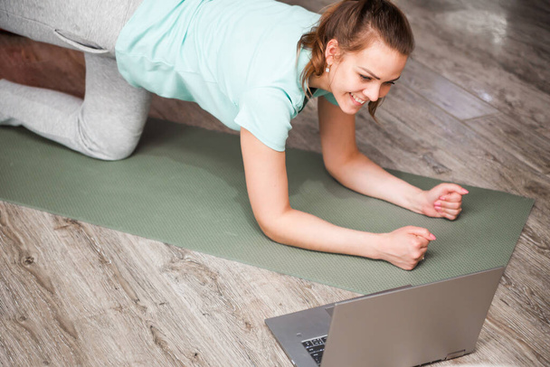 Young woman exercising at home in a living room. Video lesson. Young woman repeating exercises while watching online workout session. Beautiful young woman doing fitness exercise at home. Horizontal photo - Фото, зображення