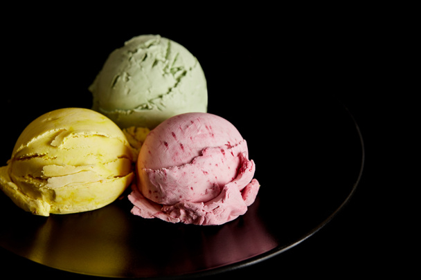 finom sárga, rózsaszín és zöld fagylaltgolyók a tányéron elszigetelt fekete - Fotó, kép