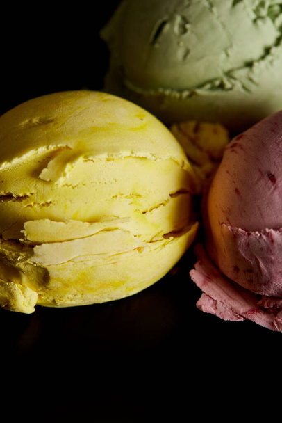 close up view of delicious yellow, pink and green ice cream balls isolated on black - Fotó, kép