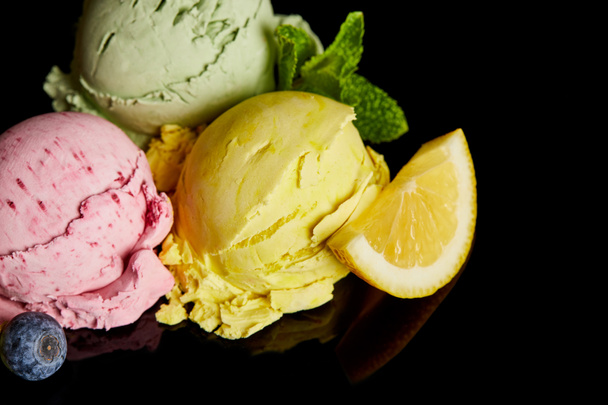 köstliche Eiskugeln aus Zitrone, Beere und Minze isoliert auf schwarz - Foto, Bild