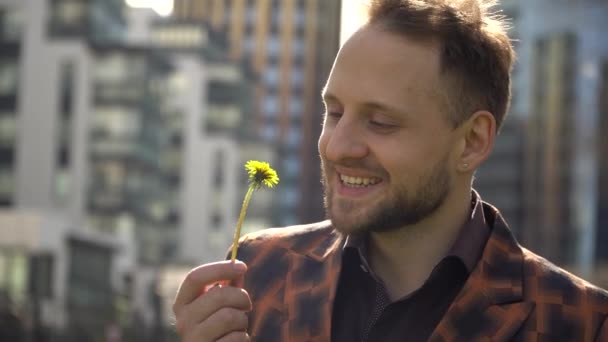 Portrait of a joyful young man who sniffs a flower, twists it and enjoys life. the concept of peace of mind. - Imágenes, Vídeo