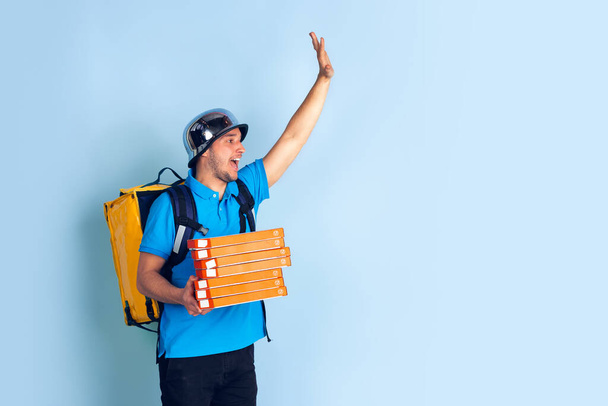 Contacless delivery service during quarantine. Man delivers food and shopping bags during insulation. Emotions of deliveryman isolated on blue background. - Foto, Bild