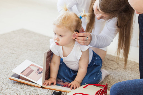 赤ちゃんの女の子の補聴器は耳。幼児は家で補聴器をつけています。障害児、障害者、難聴の概念. - 写真・画像