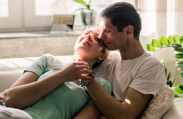 Młoda i piękna kaukaska para odpoczywa razem w domu, szczęśliwy mężczyzna i kobieta leżą na łóżku i przytulają się, harmonijne związki. Zdjęcie poziome - Zdjęcie, obraz