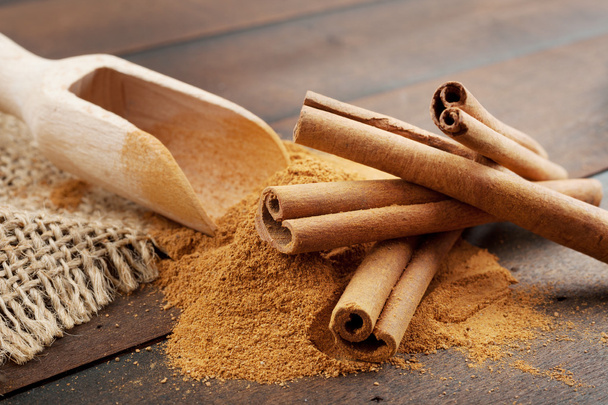 Cinnamon sticks and cinnamon powder in wooden scoop, on table - Fotó, kép