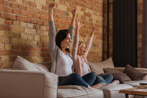 Cheerful mother with daughter watching tv on couch at home  - Foto, Imagem