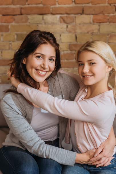 Smiling mother and daughter looking at camera while embracing on couch  - Foto, immagini