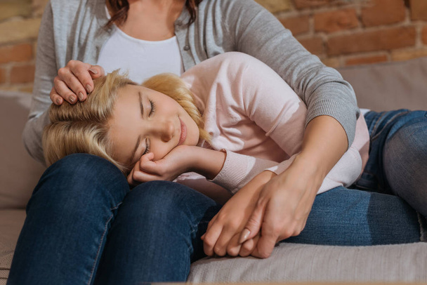 Child with closed eyes lying on couch near mother  - Фото, зображення