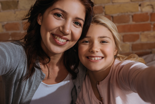 Happy mother and daughter smiling at camera at home  - Photo, Image