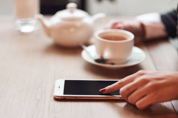 Manos de mujer con teléfono inteligente, auriculares y taza de té. Para montaje gráfico de pantalla - Foto, Imagen