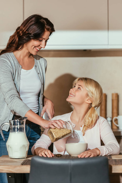 Selective focus of kid and mother smiling at each other during breakfast in kitchen  - Foto, Bild