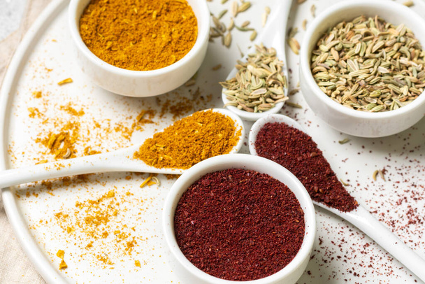 Spices and condiments in white cups and spoons on a light gray table.Fennel, sumac, Curry in white masks. Spices close-up with space for text. The view from the top - Foto, Imagen