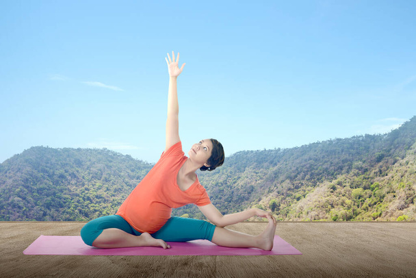 Asian pregnant woman is practicing yoga in yoga mat with mountain background - Foto, imagen