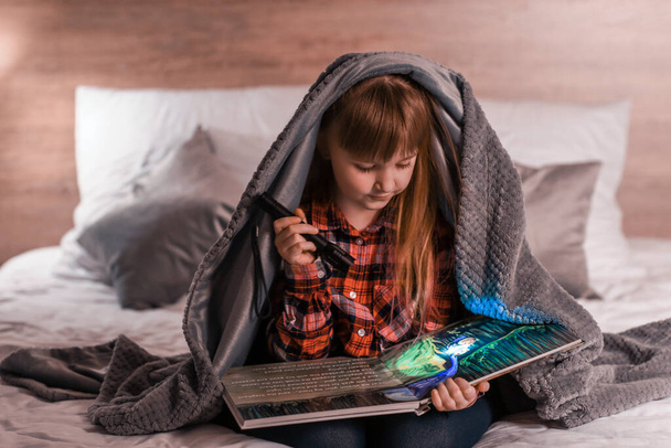 Kislány zseblámpával olvasókönyv este - Fotó, kép