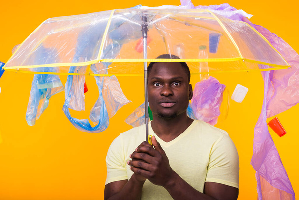 Problem of trash, plastic recycling, pollution and environmental concept - pensive african american man on yellow background with garbage. - Fotó, kép