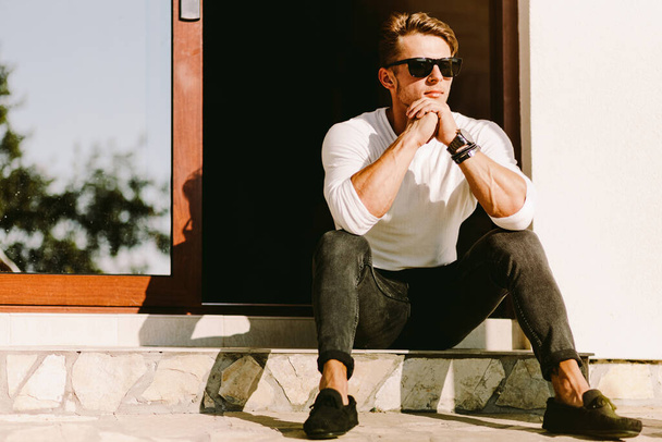 portrait of a brutal handsome man in sunglasses and watch outdoors at home. Stylish man wearing casual. Men's beauty, fashion. Optics for men. - Photo, Image