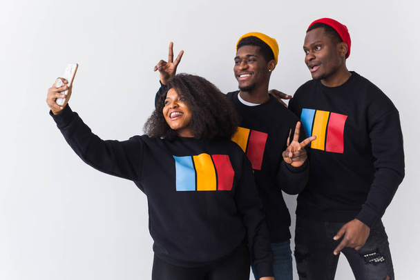 Conceito de amizade e diversão - Grupo de amigos afro-americanos homens e mulheres tomando selfie em estúdio sobre fundo branco
. - Foto, Imagem
