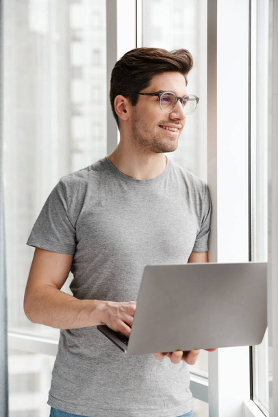 Image of a positive optimistic young man indoors at home using laptop computer. - Photo, Image