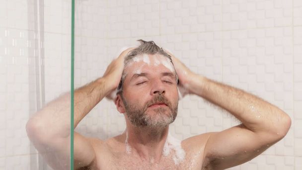 morning shower - lifestyle portrait of young attractive and happy man with beard taking a shower at home washing his hair with shampoo enjoying cheerful in wellness and hygiene concept - Фото, изображение