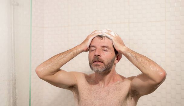 morning shower - lifestyle portrait of young attractive and happy man with beard taking a shower at home washing his hair with shampoo enjoying cheerful in wellness and hygiene concept - Fotografie, Obrázek